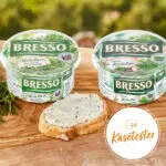 Kräuterfrischkäse von Bresso in zwei Sorten; mit Frischkäse bestrichenes Brot im Vordergrund